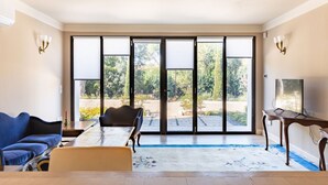 A spacious room with a large sliding glass door leading to an outdoor area, a dining table, a sofa, and a television on a wooden stand.