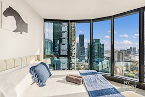 Enjoy a panoramic city view from the large window in this stylish room, featuring a comfortable bed and minimalist artwork.