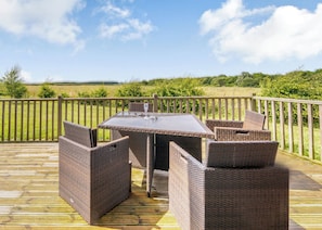 A deck with a table and wicker chairs, overlooking a grassy field.