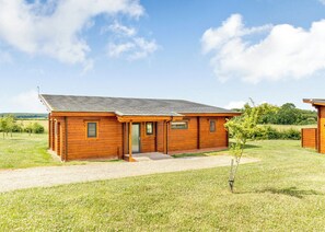 A wooden cabin with a porch, a gravel driveway, and a grassy field.