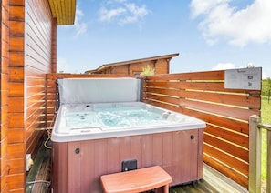Un bain à remous doté d’une terrasse en bois et d’un banc, le tout entouré de murs en bois.