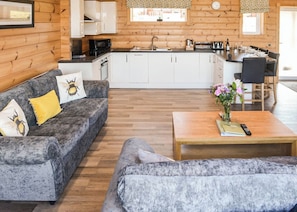 Un salon chaleureux avec un canapé gris, une table basse et un coin cuisine doté de meubles blancs et d’un plancher en bois.