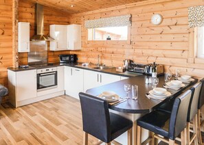 A wooden cabin interior with a kitchen, dining area, and a clock on the wall.