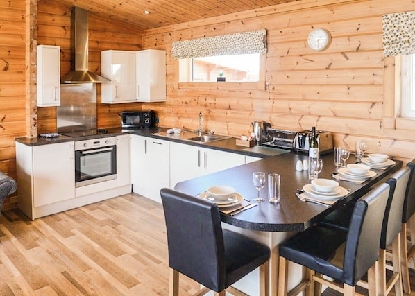 Interior de una cabaña de madera con cocina, comedor y un reloj en la pared.