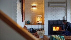 A cozy living room with a fireplace, a white brick wall, and a person sitting on the floor. - The Arthouse Freycinet (Glamorgan-Spring Bay)