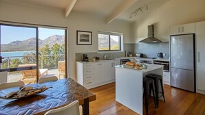 A modern kitchen with a large island, white cabinetry, and a view of the sea. - The Arthouse Freycinet (Glamorgan-Spring Bay)