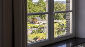 A view through a window of a house with a garden, a wooden structure, and a lawn. - La chocolaterie de Roly (Philippeville)