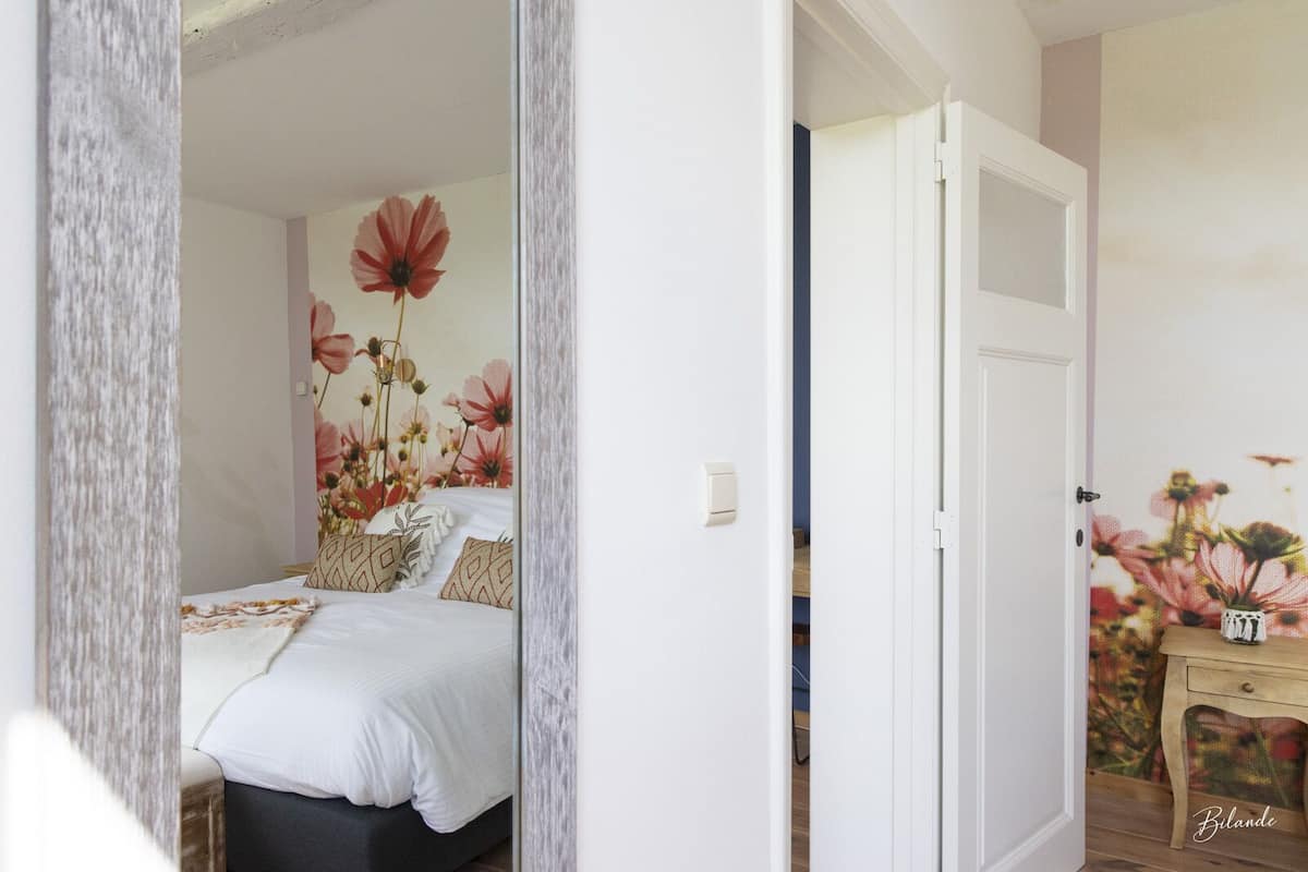 A bedroom with a bed, a nightstand, and a wall with a floral mural.