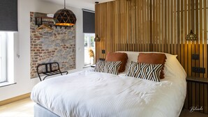 A bedroom with a large bed, a stone wall, wooden slats, and hanging lamps. - La chocolaterie de Roly (Philippeville)