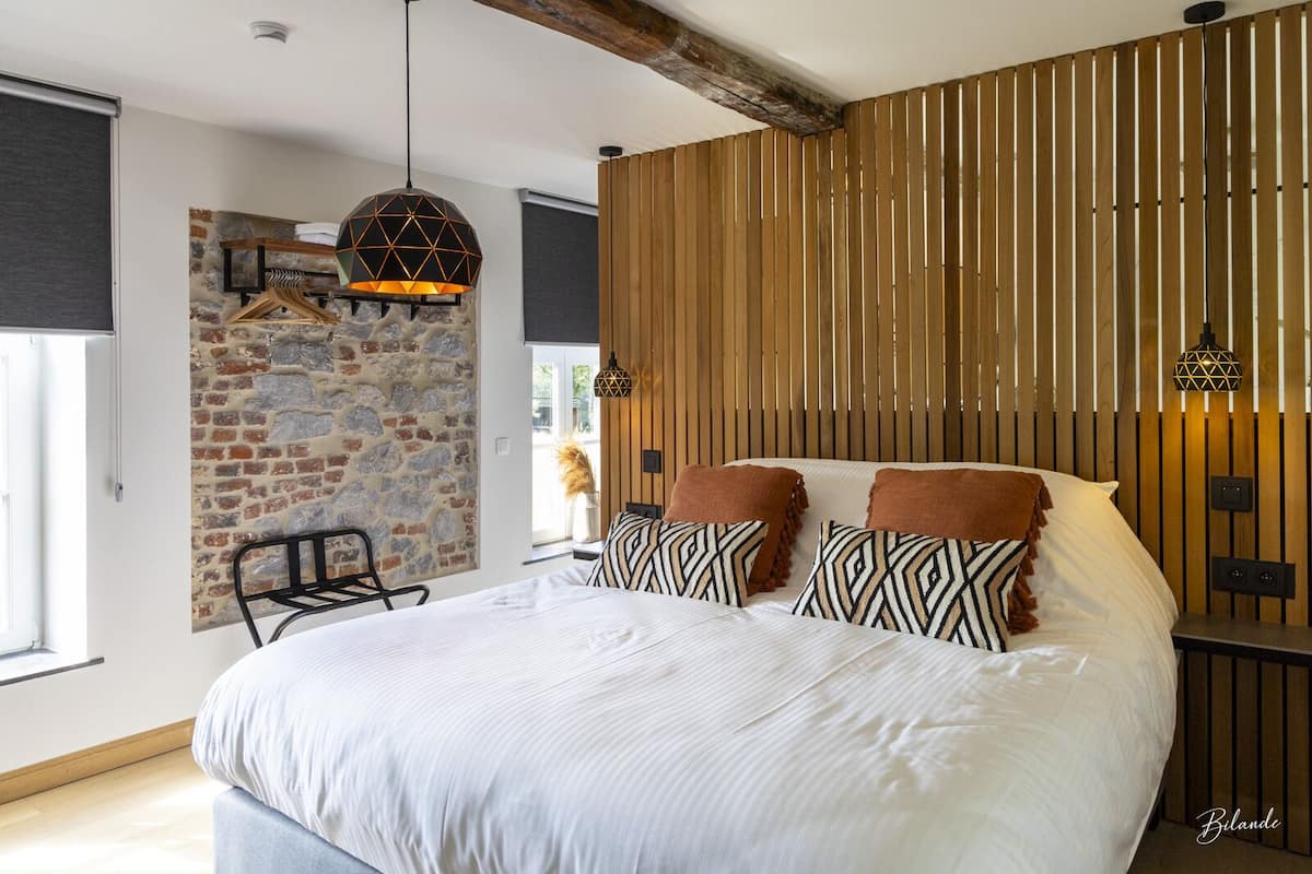 A bedroom with a large bed, a stone wall, wooden slats, and hanging lamps.