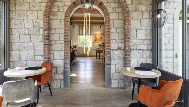 A spacious interior with a stone archway leading to a dining area, wooden flooring, and modern lighting fixtures. - La chocolaterie de Roly (Philippeville)