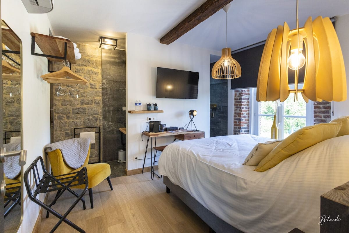 A bedroom with a bed, a desk, a chair, a TV, and a stone wall.