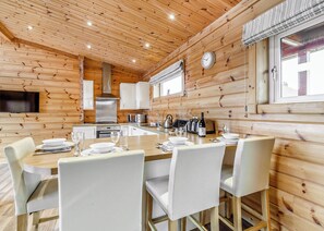 Een houten blokhut van binnen met een eettafel voor vier personen, een keuken met moderne apparatuur en een groot raam.
