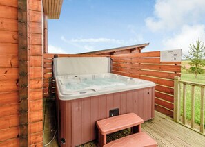 Un jacuzzi en una terraza de madera con un banco, rodeado por una valla de madera y un cielo despejado.