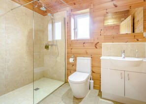 Un baño con cabina de ducha de vidrio, inodoro y lavamanos, con paneles de madera en las paredes.