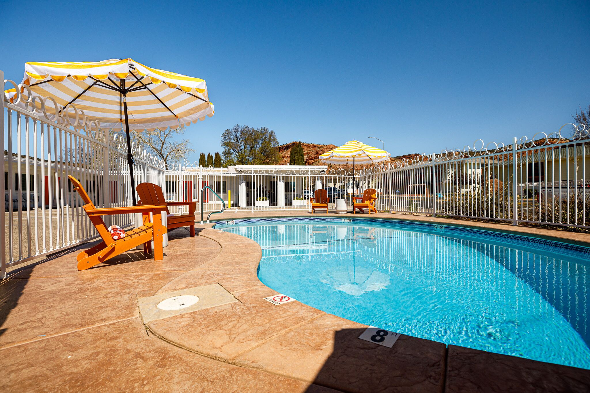 A swimming pool with a white fence, lounge chairs, and striped umbrellas.