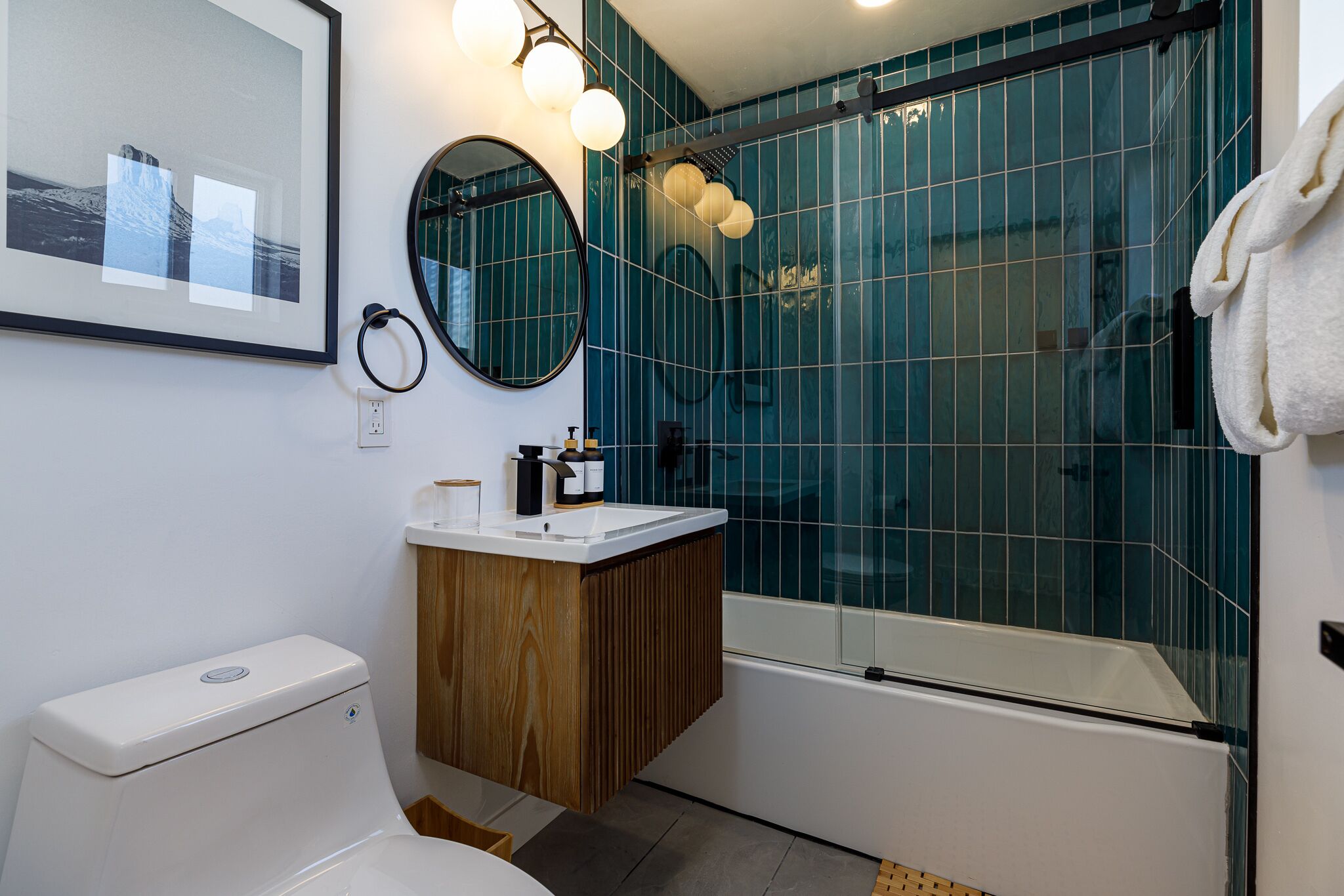 A modern bathroom with a toilet, sink, mirror, and shower area.