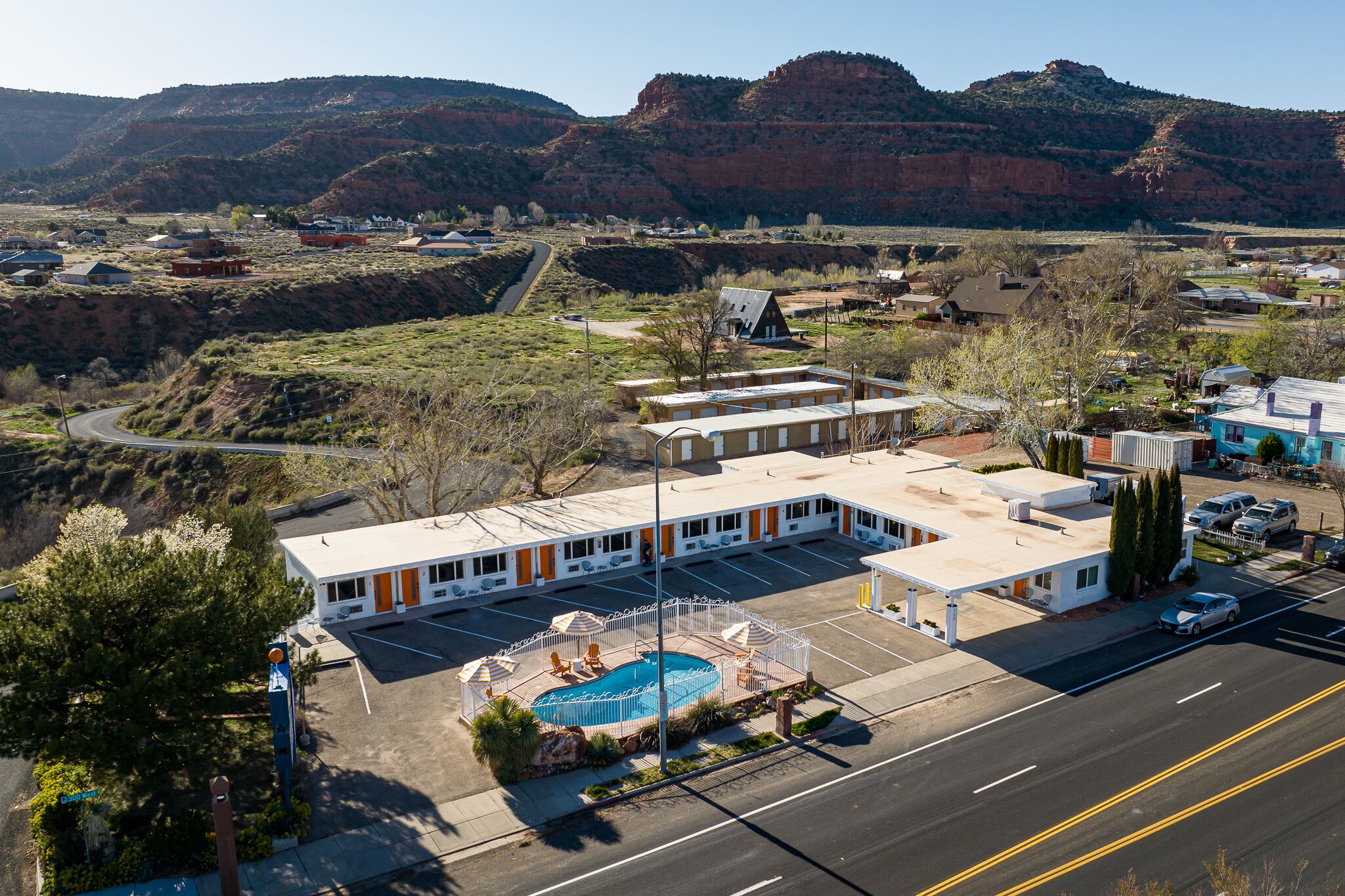 A motel with a swimming pool, parking lot, and a view of the surrounding hills.