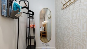 Un baño con espejo, perchero, repisa con artículos de aseo y cama para mascotas.