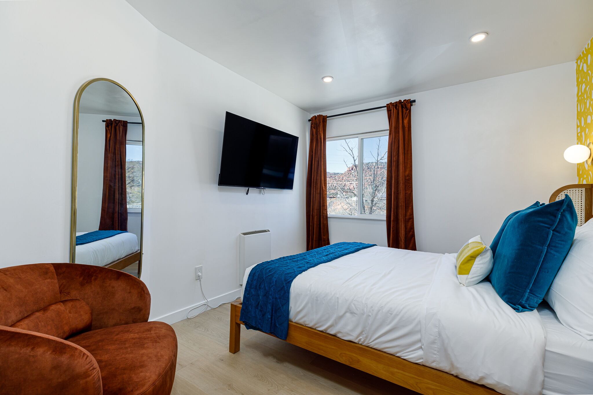Un dormitorio con cama, televisor, espejo y ventana con cortinas.