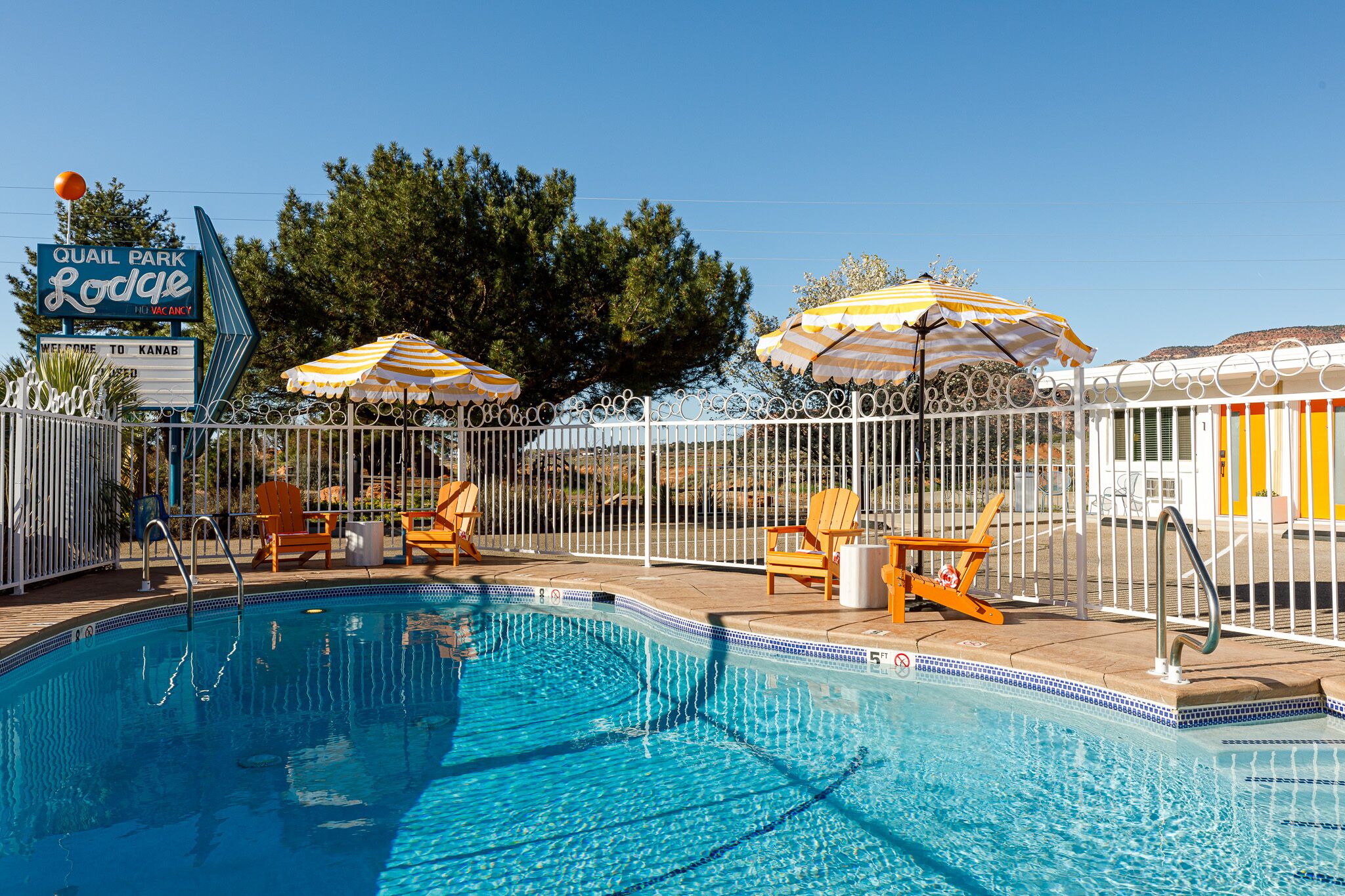 A swimming pool with lounge chairs and umbrellas, surrounded by a white fence.