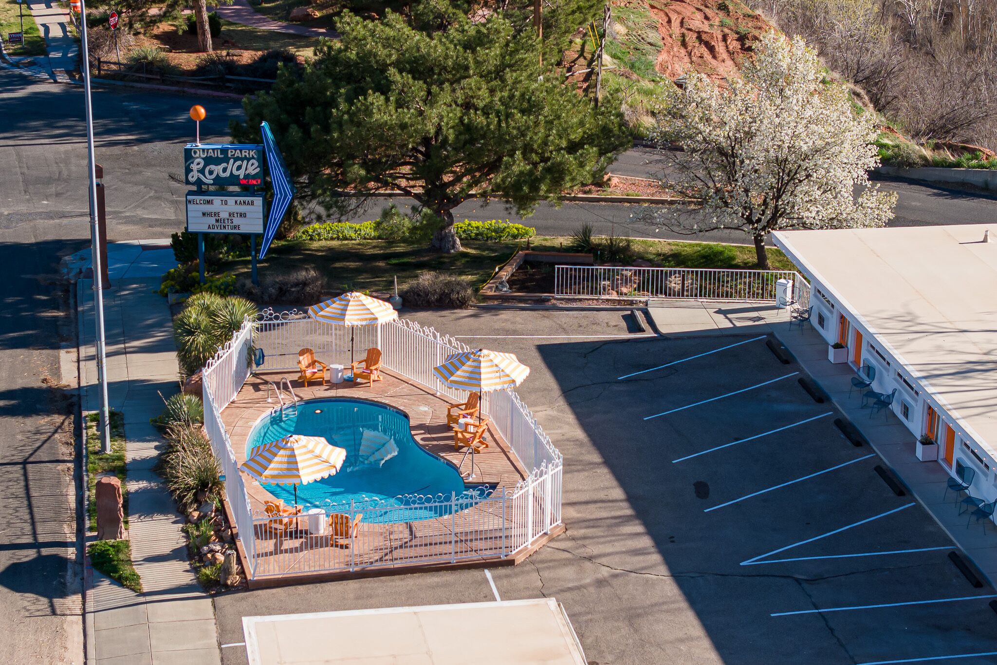 A pool area with a sign for Quail Park Lodge, a fenced pool with lounge chairs, and a parking lot.