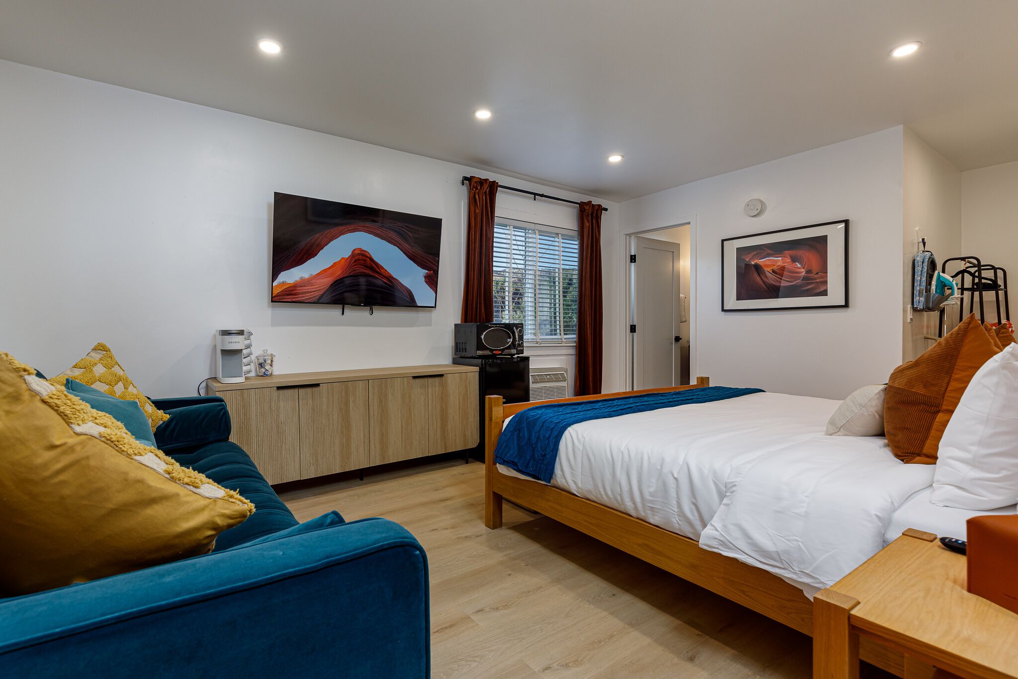 Una habitación de hotel moderna con cama, sofá, escritorio y una kitchenette pequeña.
