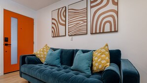 Una sala de estar moderna con un sofá color turquesa, almohadones estampados amarillos y arte abstracto en la pared.