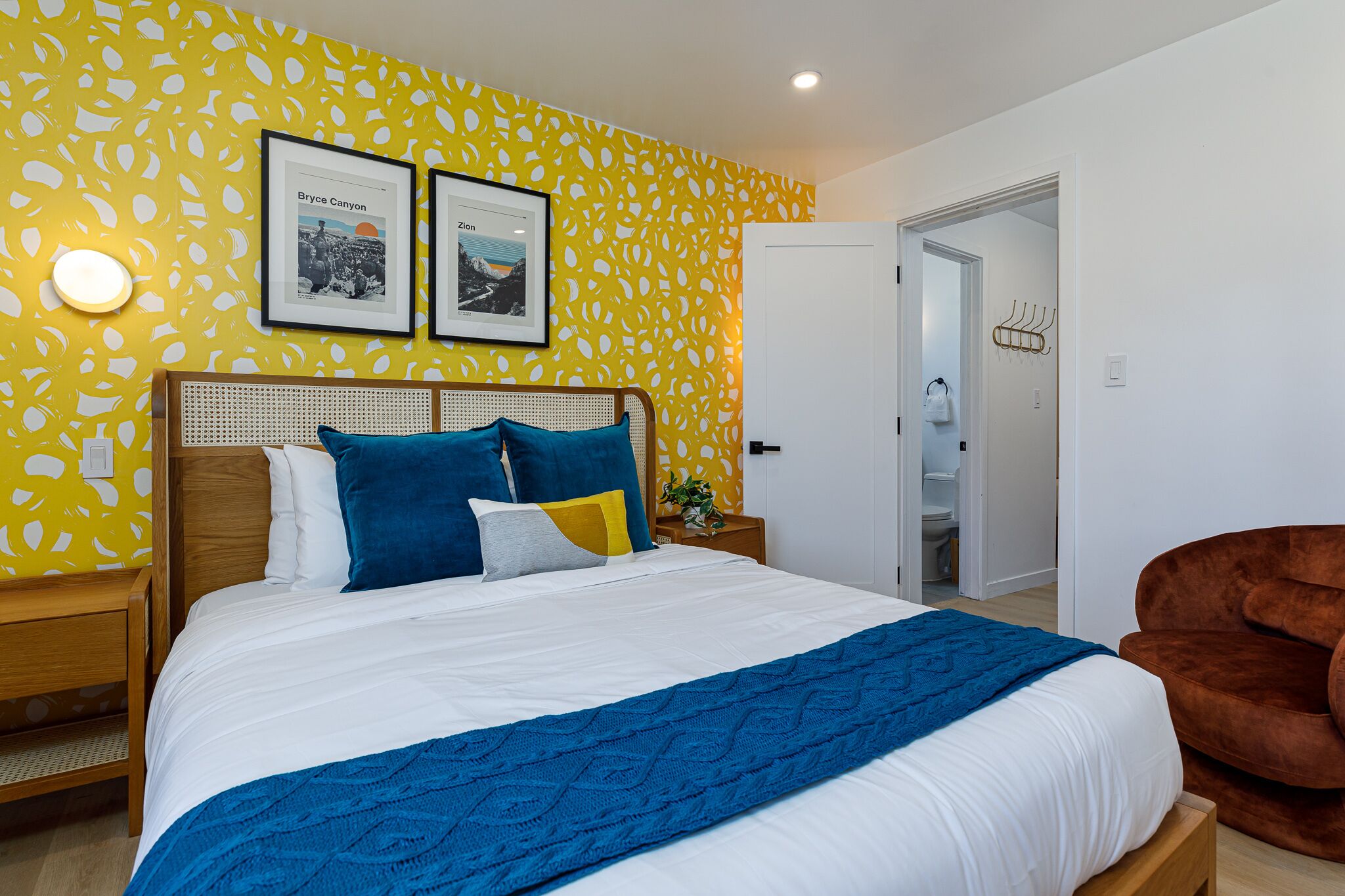 A bedroom with a bed, a nightstand, a chair, and a door leading to a bathroom.