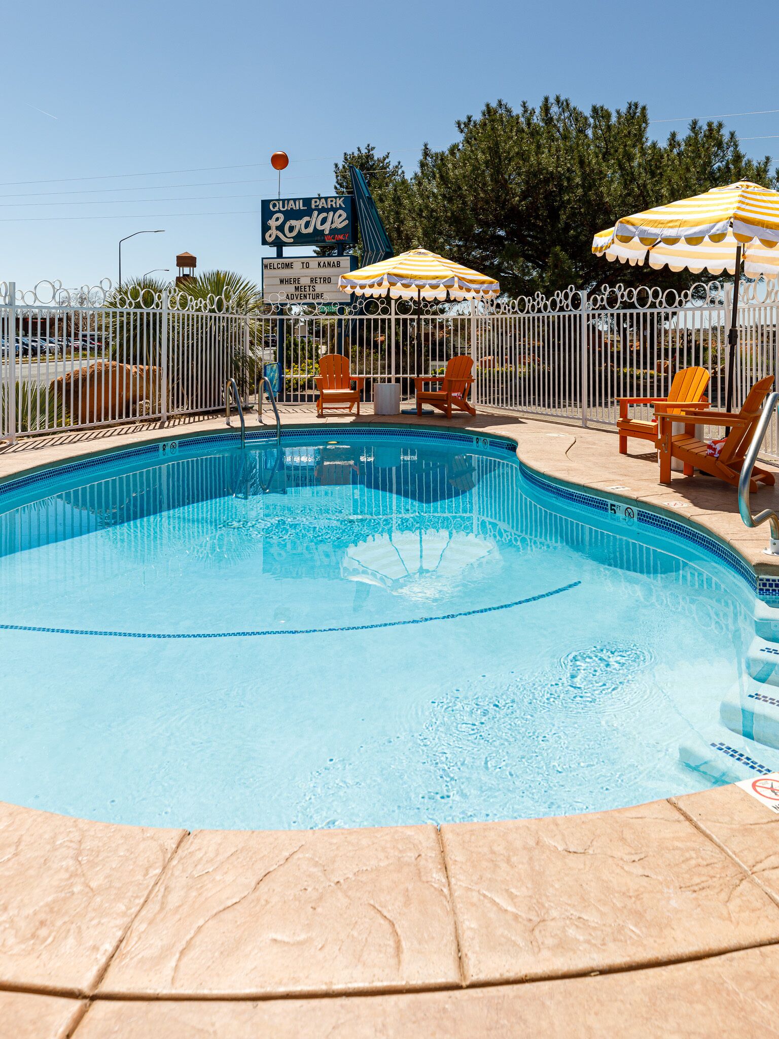 Una piscina con sillas de descanso y sombrillas, rodeada por una valla.
