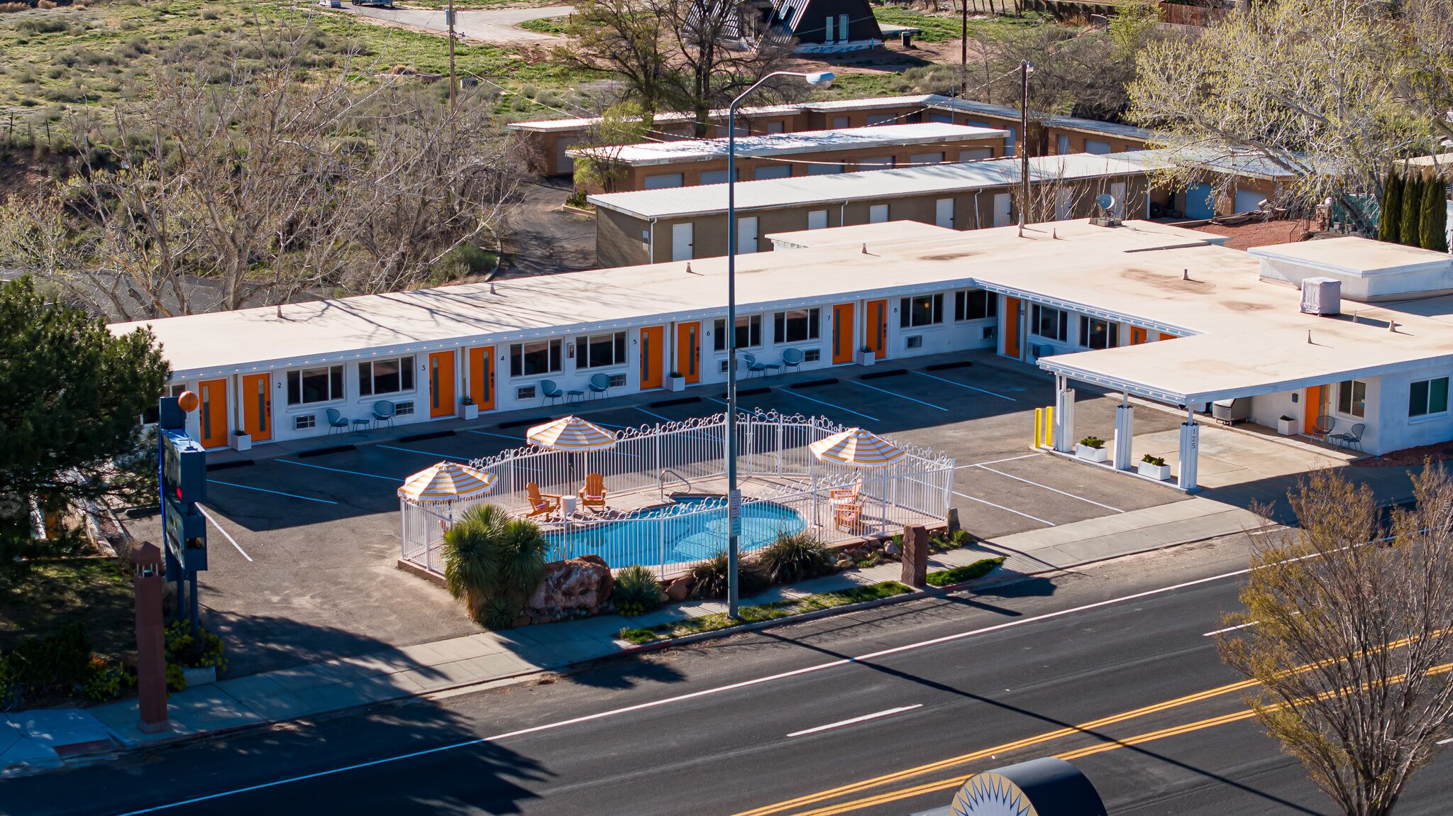 A motel with a swimming pool, outdoor seating, and a parking lot.