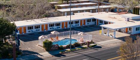 A motel with a swimming pool, outdoor seating, and a parking lot.