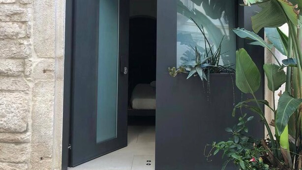 A modern building entrance with a glass door marked '53', a dark interior visible through the door, and a large potted plant to the right. - Locus Pendinelli Trani 53-the Philosophy of a B&b, the Details of a Hotel!!! (Trani)