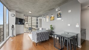 Ein modernes Wohnzimmer mit grauem Sofa, einem Glastisch und einem großen Fenster.