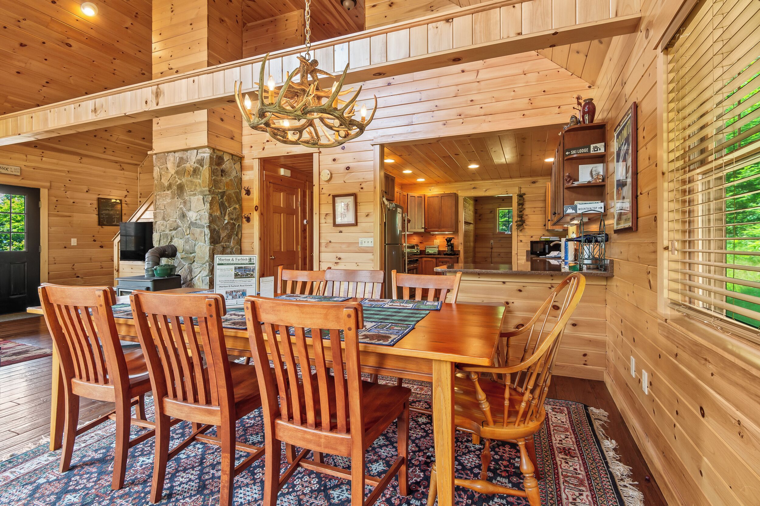 A wooden interior with a dining area, stone fireplace, and kitchen.