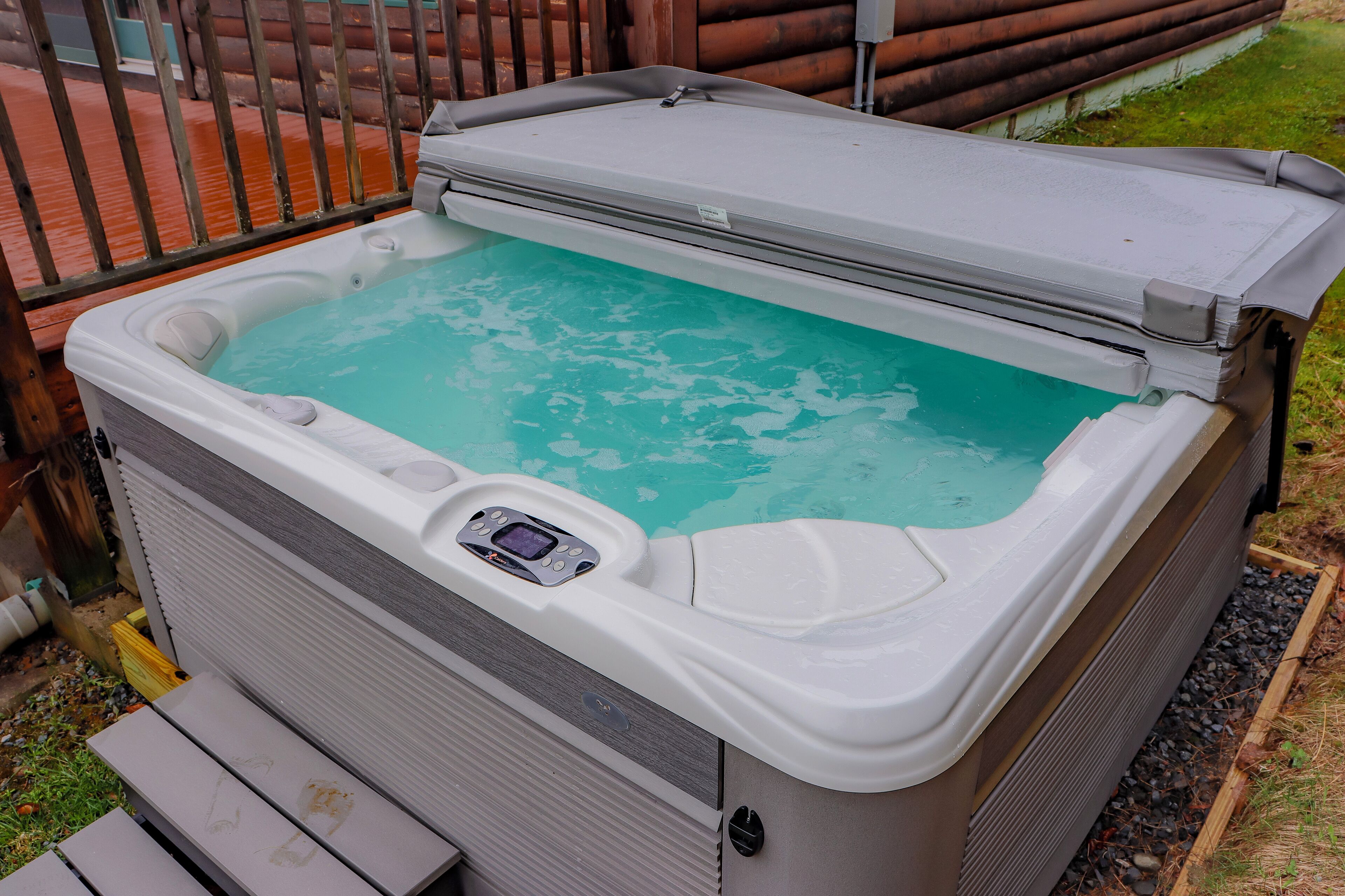 Un jacuzzi con panel de control, rodeado por una cubierta de madera y una valla metálica.