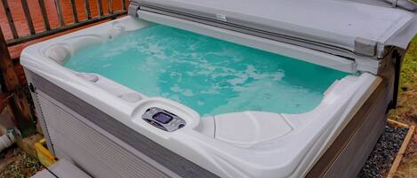 Un jacuzzi con panel de control, rodeado por una cubierta de madera y una valla metálica.