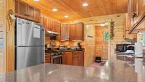 A modern kitchen with wooden cabinets, stainless steel appliances, granite countertops, and a wooden ceiling. - Whippoorwill - Wooded location, hot tub, close to downtown Oquossoc (Rangeley)