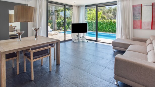 A modern living room with a pool view, a flat-screen TV, and a dining area. - Holiday Home 'Sunny House' with Sea View, Wi-Fi and Air Conditioning (Sant Pere de Ribes)