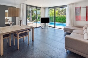 Una sala moderna con vista a la piscina, un televisor de pantalla plana y un comedor.