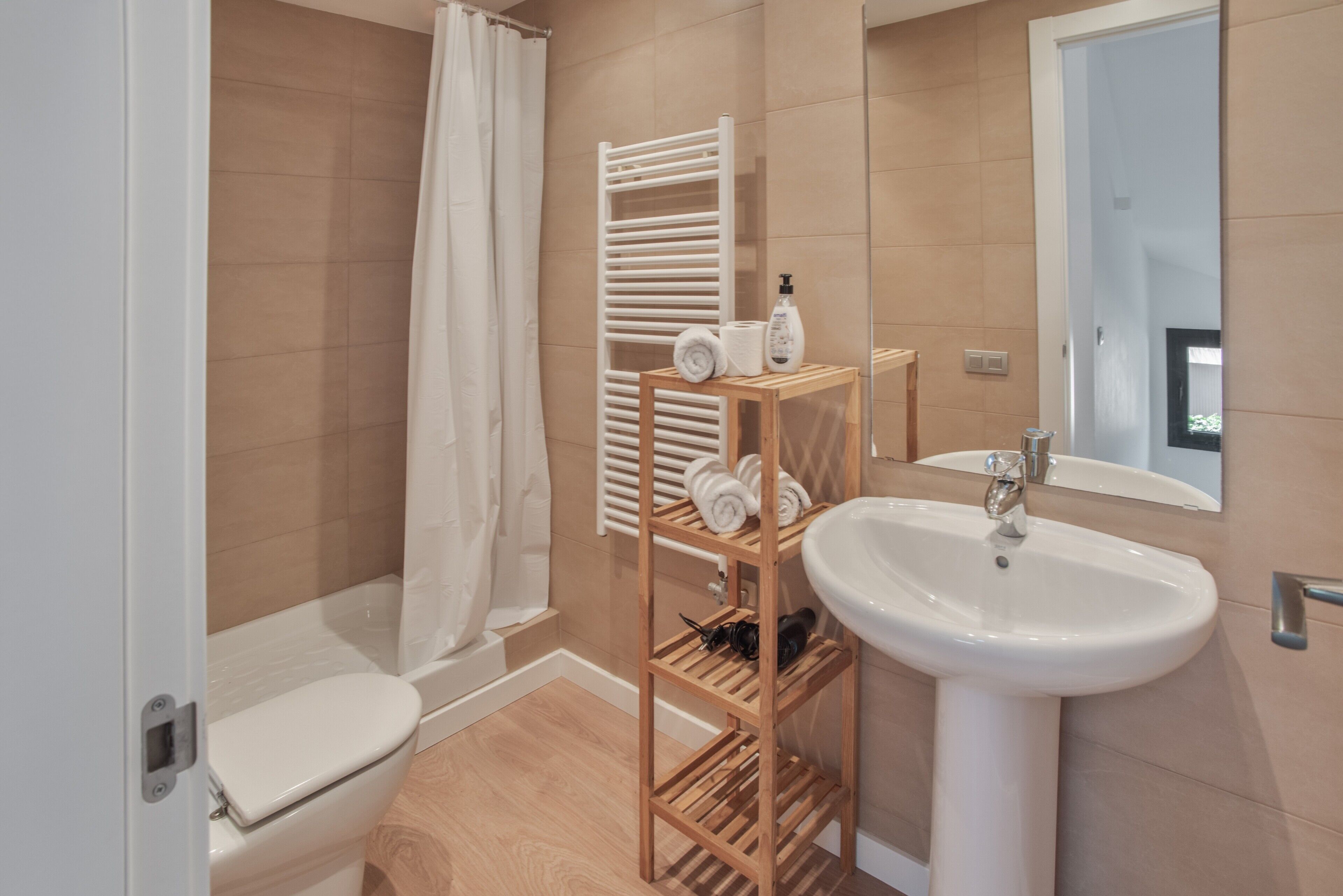 Une salle de bain moderne équipée de toilettes, d’une douche, d’un porte-serviettes en bois, d’un lavabo et d’un miroir.