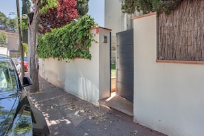 Una calle estrecha con un coche estacionado, un edificio con una puerta y un árbol con follaje verde.