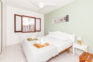 Un dormitorio con cama, mesita de noche, lámpara, ventana con cortinas y ventilador de techo.