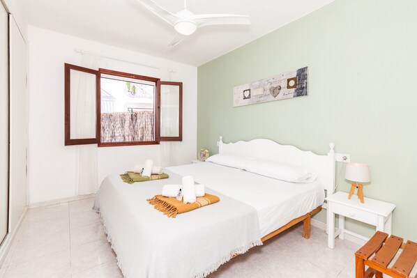 A bedroom with a bed, a nightstand, a lamp, a window with curtains, and a ceiling fan.