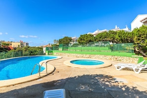 A swimming pool with two separate sections, a green fence, and lounge chairs.