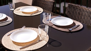 Een tafel gedekt met borden, bestek en glazen, omringd door rieten stoelen.