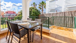 Een balkon met een eettafel voor vier personen, een groene balustrade en uitzicht op gebouwen en bomen.