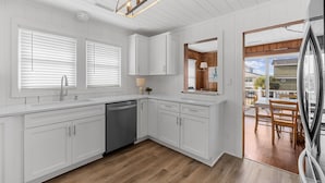 Une cuisine moderne avec des meubles blancs, un lave-vaisselle et un coin repas comprenant une table et des chaises en bois.