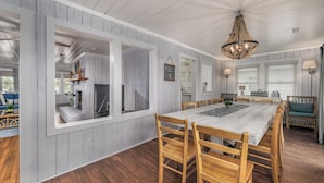 Un espace repas avec une grande table et des chaises en bois, des murs blancs et un lustre.