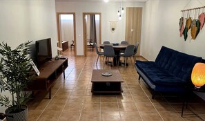 A living room with a TV, sofa, coffee table, and dining area with chairs.